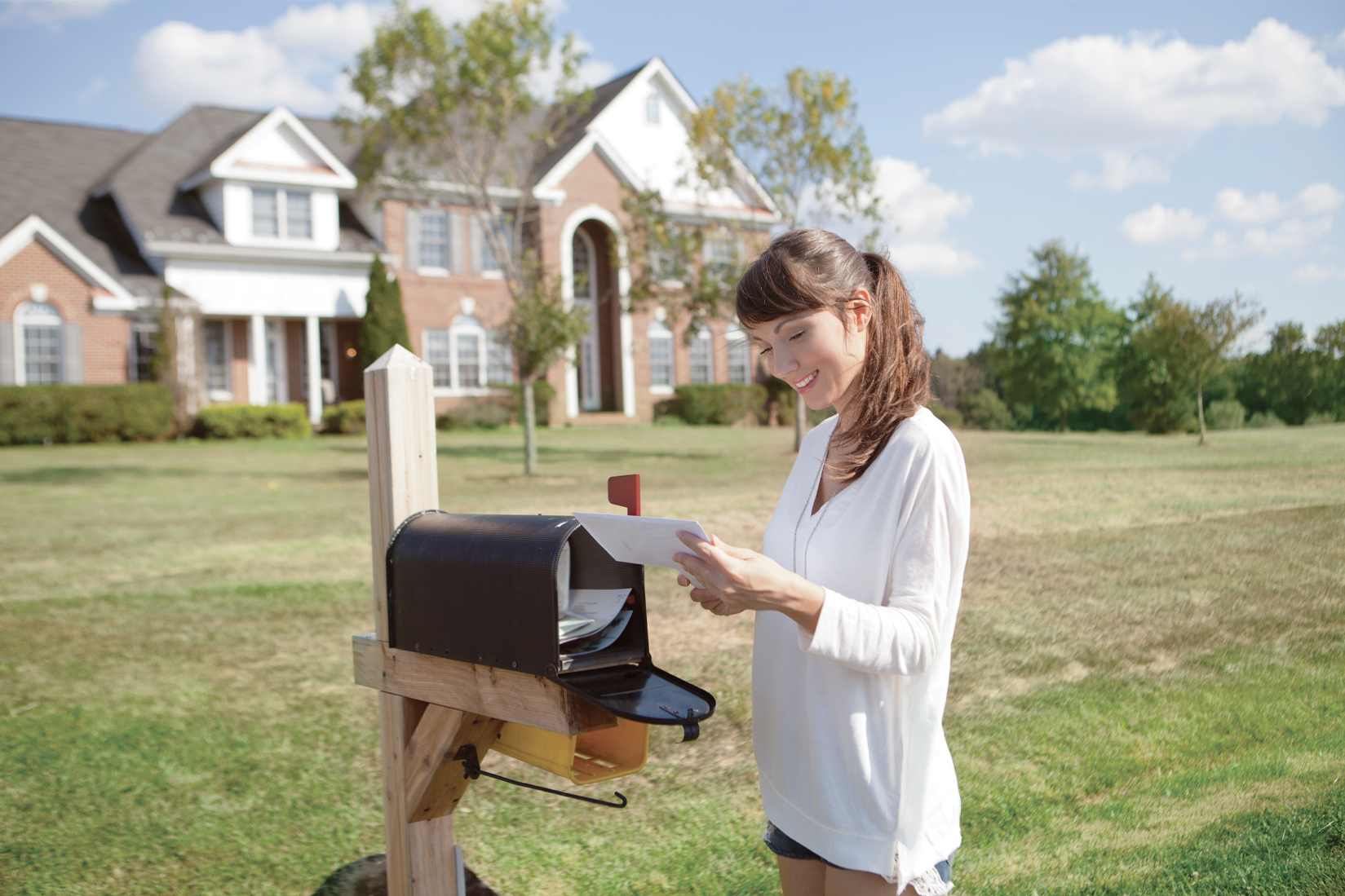 An adult woman checking the mail at the mailbox in front of her home on a sunny day