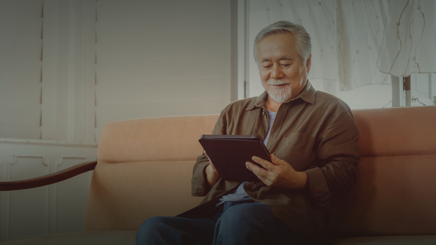An older man sitting on the couch looking at his tablet