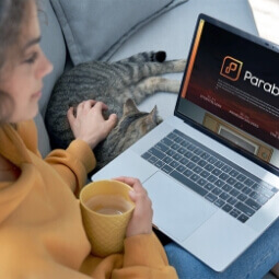 A girl with her laptop on her lap holding coffee and petting a cat