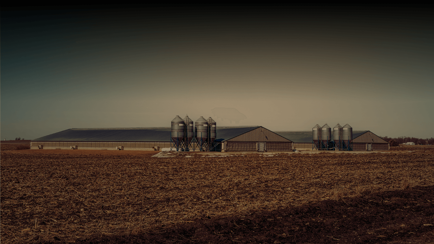 A large farm field after the harvest with grain storage in the background.