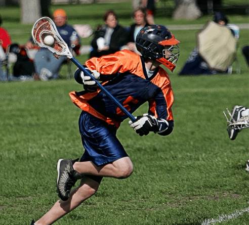 A male lacrosse player running down the field cradling the ball in his stick